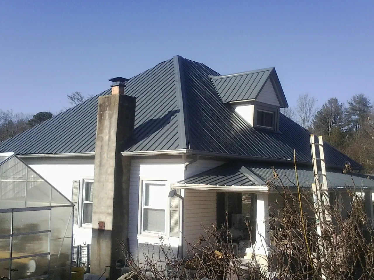 Dark blue standing seam metal roof on a white farmhouse with dormer — Slate & Tile Roof Repair by Roofing Brothers in Colonial Heights