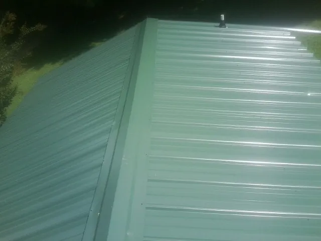 New green metal panels meeting at the ridge of a roof — Flat Roof Repair work by our crew in Colonial Heights