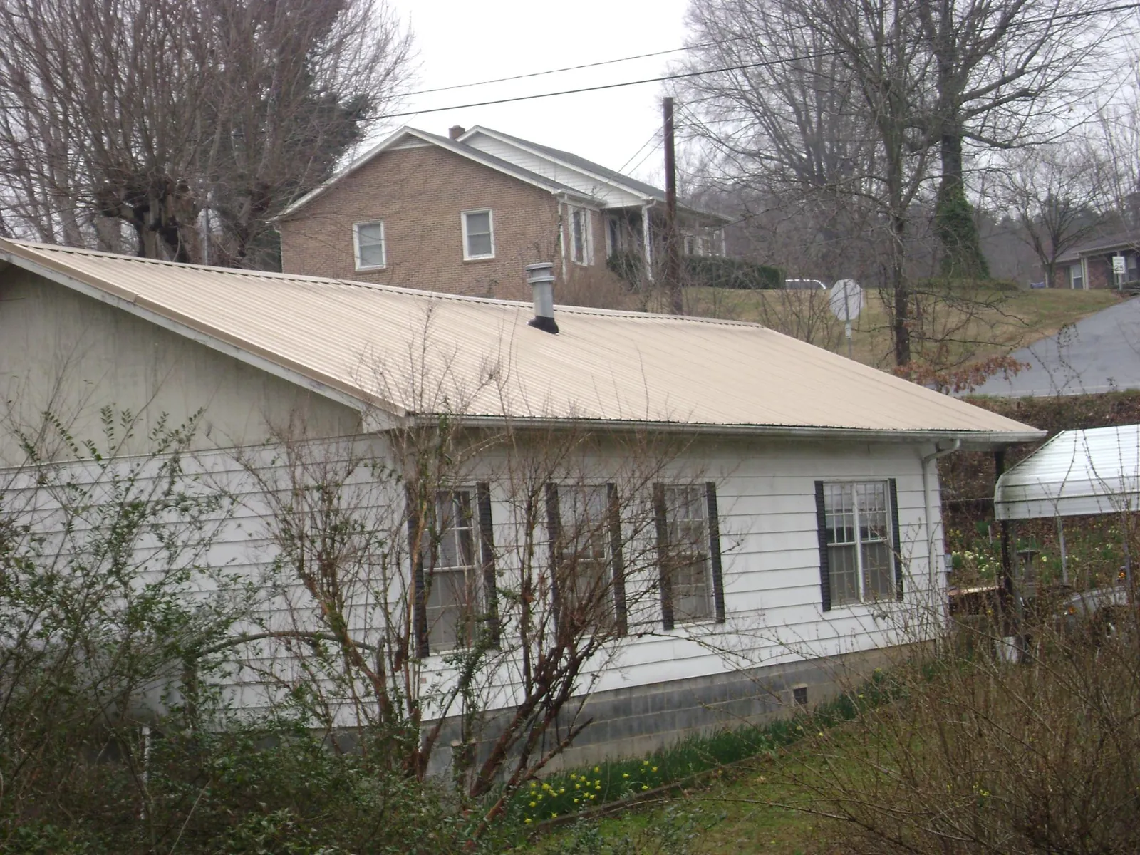 Tan metal roof on a white sided house set into a hillside — Commercial Roofing by Roofing Brothers in Colonial Heights